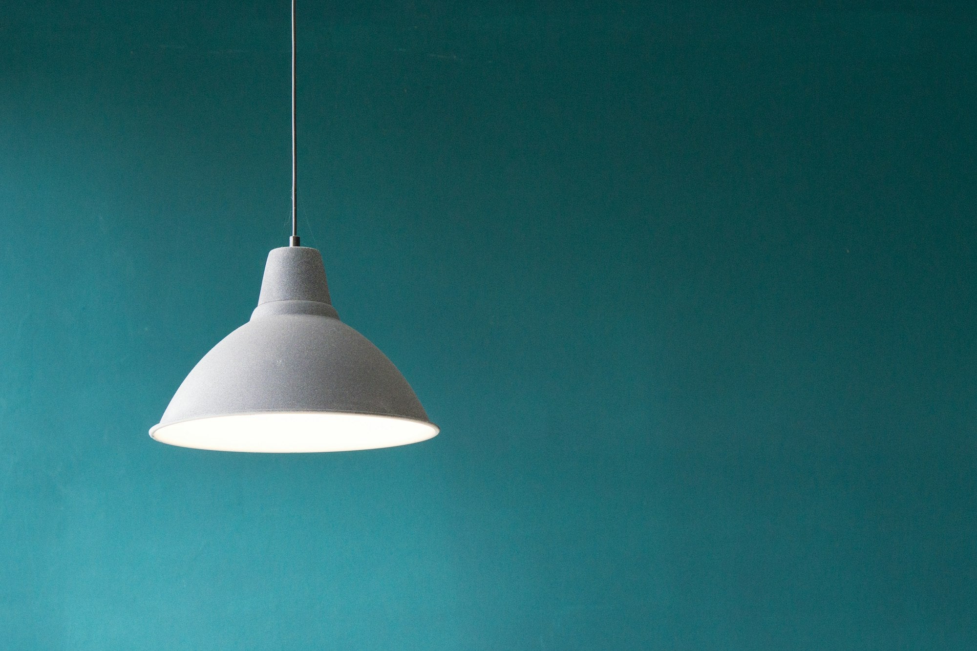 Pendant lamp glowing against a teal wall